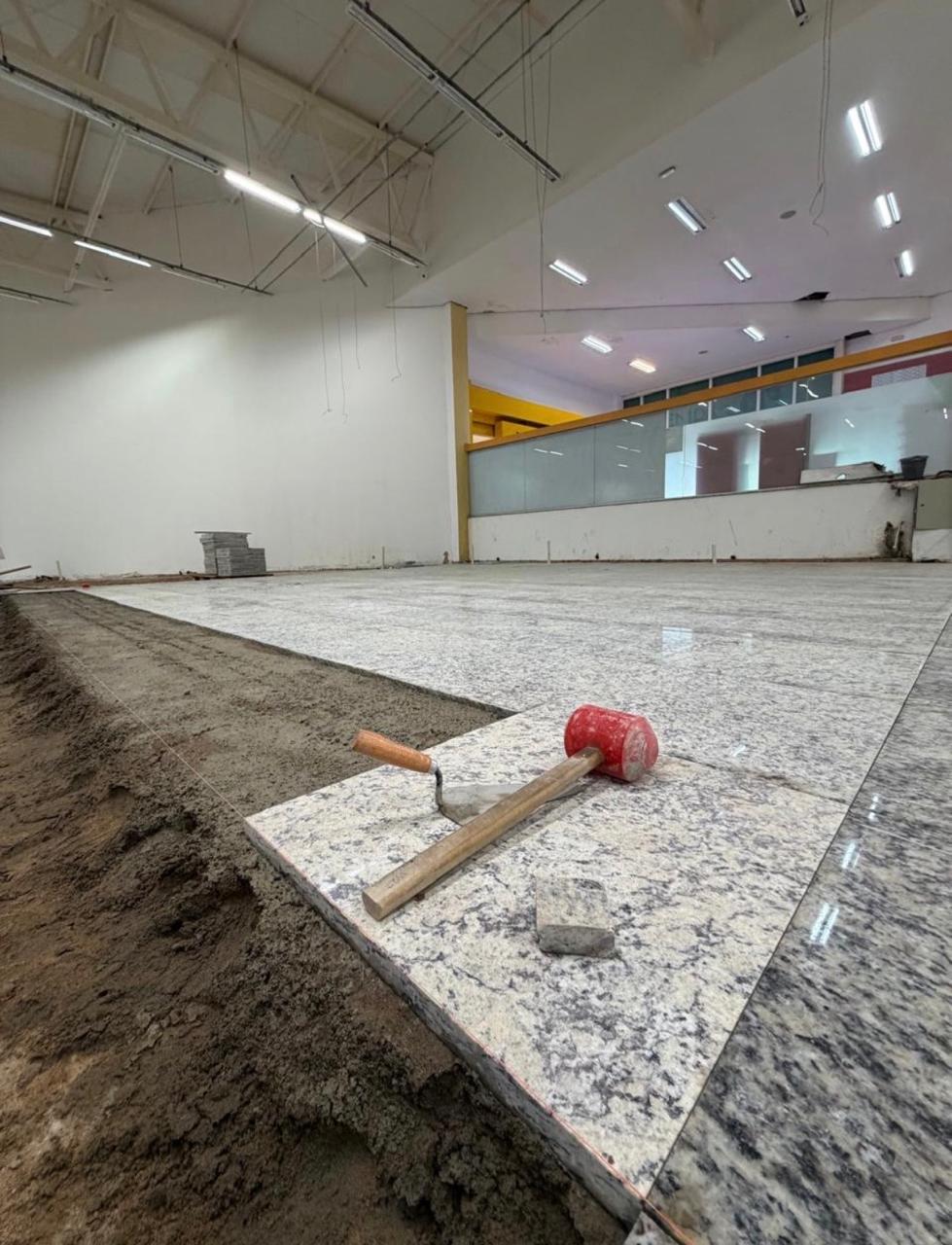 Piso de granito sendo assentado sobre a farofa, com martelo de borracha vermelho